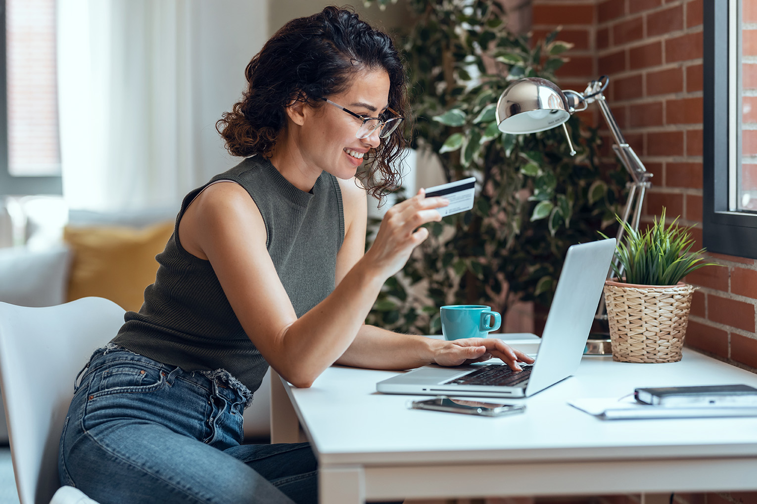 Woman sitting in front of her laptop holding her credit card in her hands.