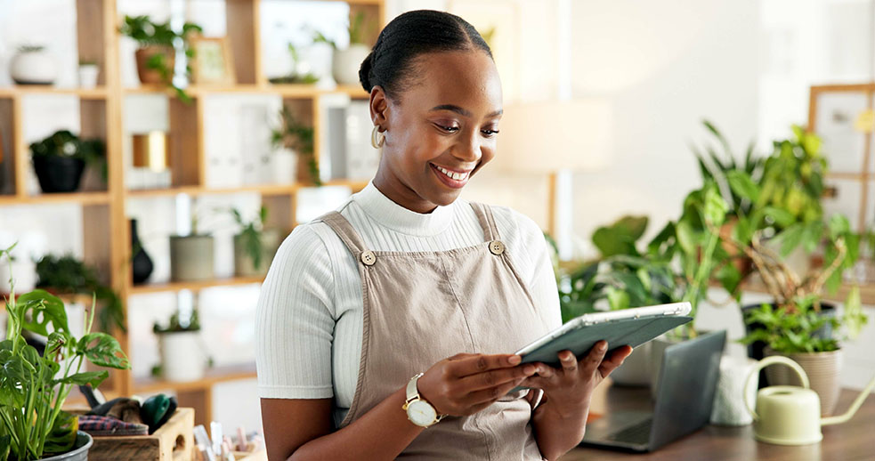 Smiling young woman surrounded by greenery using a tablet