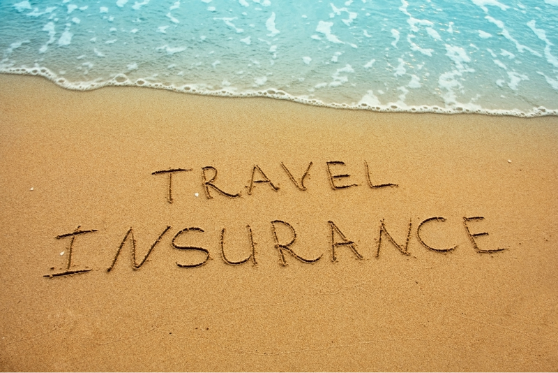 travel insurance written on the sand of a beach