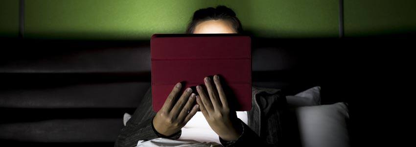 A person reading with a tablet on the bed at night