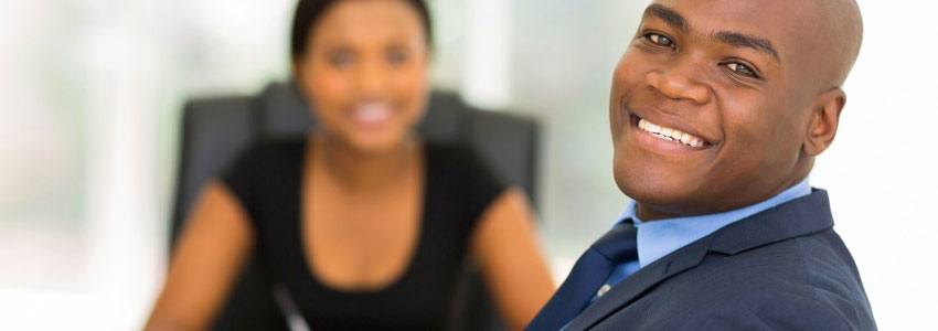 A man smiling with a woman sitting in the background