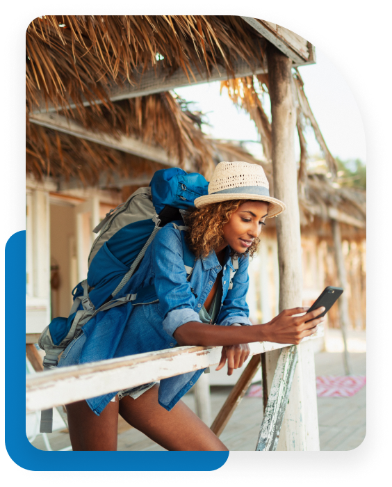 Young woman backpacking in a hot country, taking a moment under a straw roof and looking at her cell phone. 