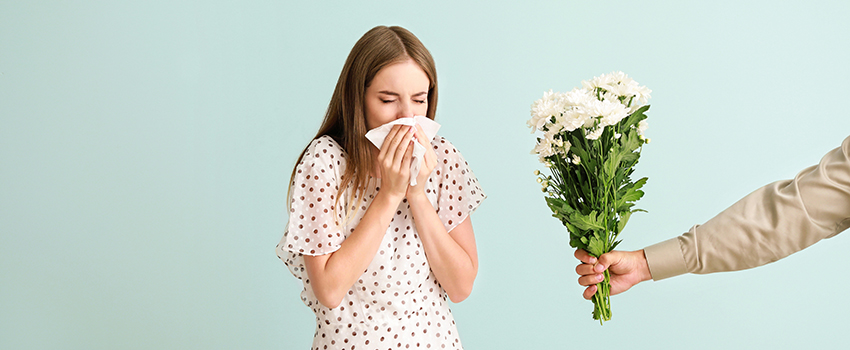 A woman sneezing into handkerchief while someone holding a bouquet of flowers