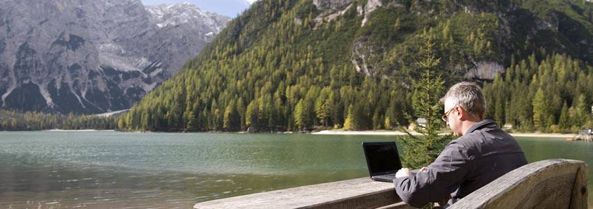 A man sitting on a bench using a computer beside a lake 