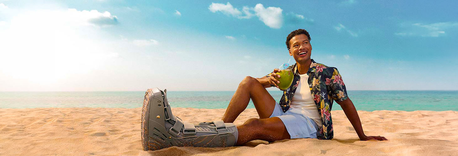 smiling young man sitting in the sand with a foot in a cast