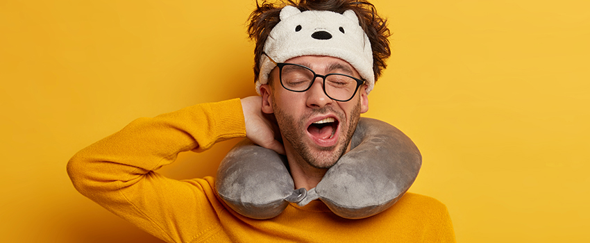 A sleepy man yawning with a neck pillow